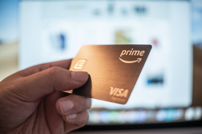 Un hombre sostiene en su mano una tarjeta Visa Signature de Amazon Prime Rewards.