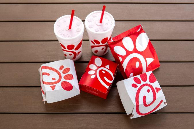 Chick fil una bolsa junto a vasos de cola, pollo con tiras y hamburguesa picante.