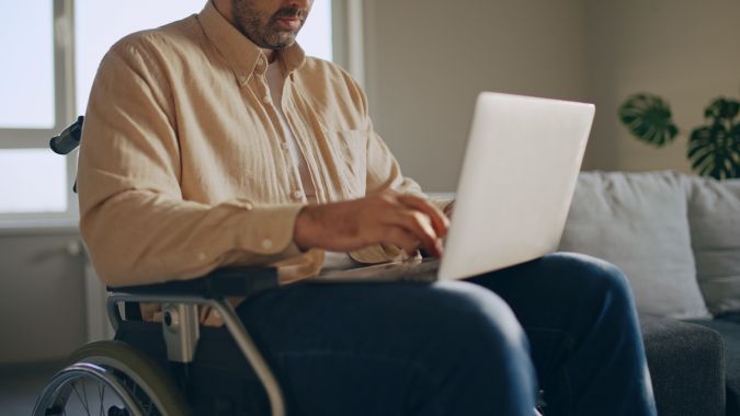 Hombre con discapacidad trabajando con una computadora portátil en silla de ruedas, trabajo independiente.