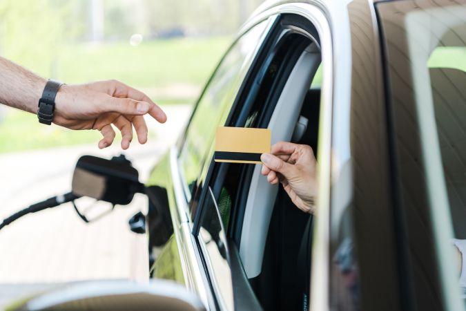 Vista recortada de una mujer en un automóvil que le da una tarjeta de crédito a un trabajador en una gasolinera.