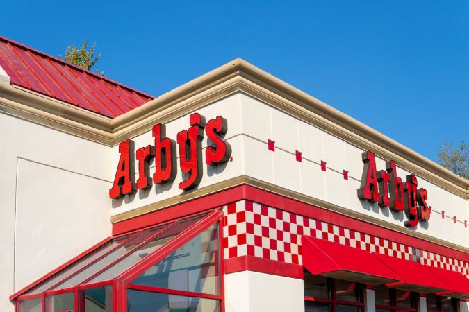 Toma horizontal de la fachada exterior del restaurante de comida rápida "Arby's" con la marca y el logotipo sobre las ventanas de vidrio en un día soleado.