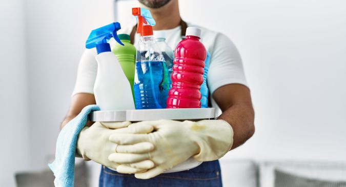 Joven hispano sosteniendo productos de limpieza en casa.