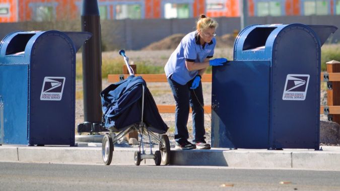 Un trabajador postal de USPS recoge el correo saliente en un buzón de entrega.