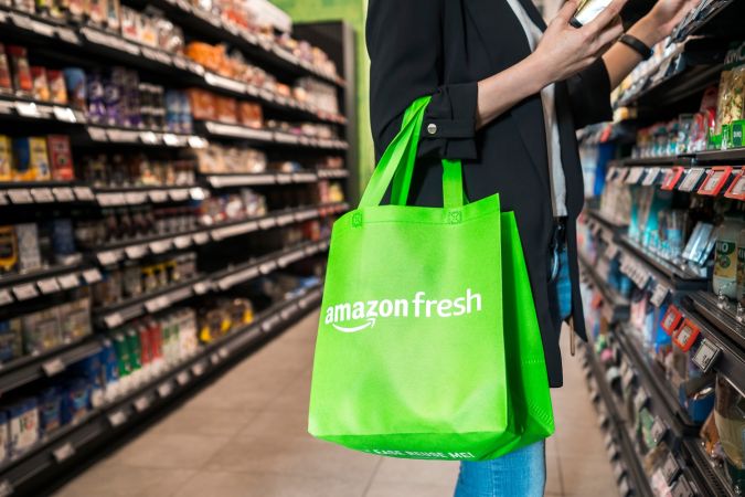 Mujer comprando solas en Amazon Fresh interior con bolsa de reciclaje verde.