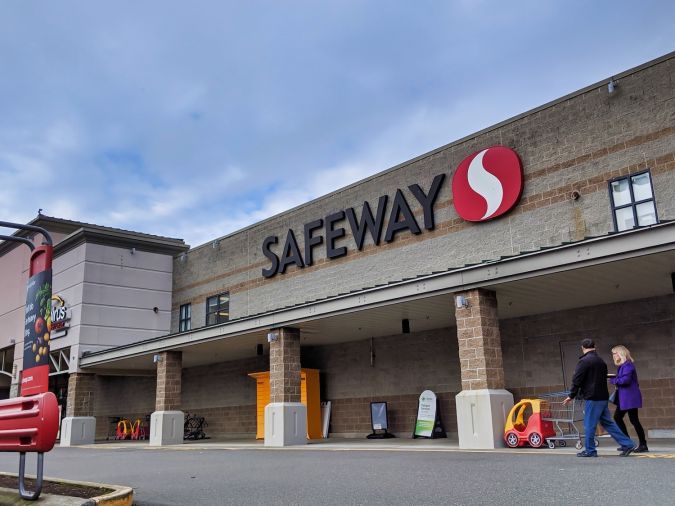 Vista de la calle de una tienda de comestibles Safeway con personas acercándose a la entrada para comprar alimentos.