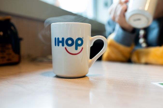 Taza Ihop con café caliente sobre una mesa con vapor saliendo de ella.