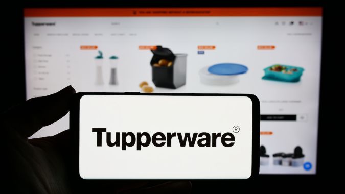 Persona que sostiene un teléfono inteligente con el logotipo de la empresa estadounidense de productos para el hogar Tupperware Brands Corporation frente a un sitio web.