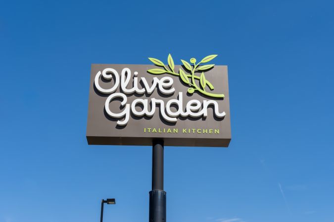 Un cartel de Olive Garden con un cielo azul de fondo.