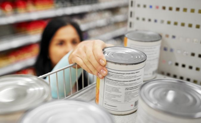 Mujer sacando una lata con comida del estante en el supermercado.